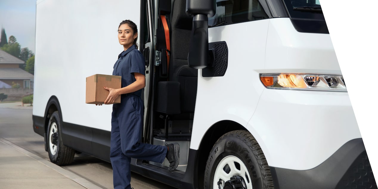 A GM delivery personnel carrying a small box exiting a 2025 Chevrolet BrightDrop EV van.
