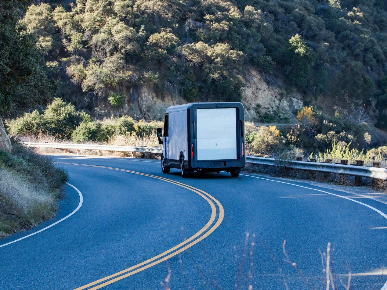 Vue latérale arrière de la fourgonnette électrique Chevrolet BrightDrop 2025 en mouvement seule sur la route.