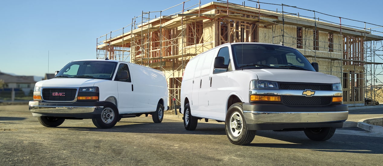A GMC Savana and a Chevrolet Express Van parked side by side on a construction site.