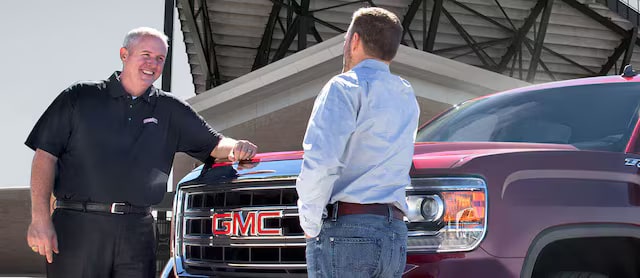 A Business Elite Dealer talking to a customer beside a GMC vehicle.
