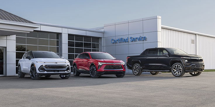 Three GM commercial vehicles parked outside a building.