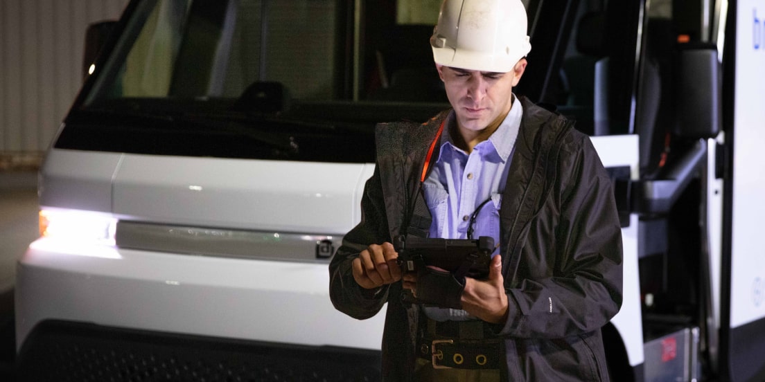 A construction worker using a tablet device near a GM Envolve vehicle.