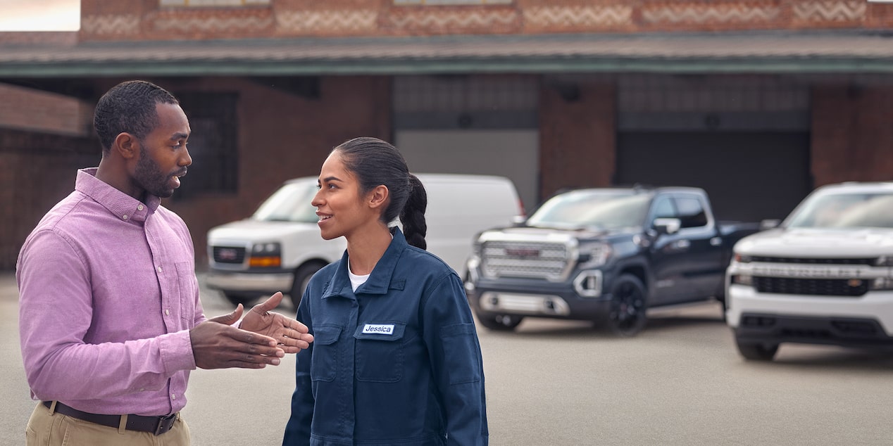 Two people talking near three GM Envolve trucks.