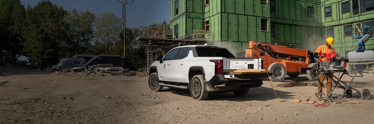 A Chevrolet Silverado EV with an open tailgate. A construction worker works near by. 