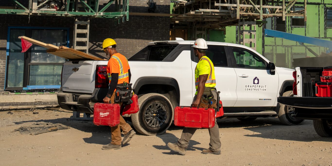 Two construction worker carrying tools out of the tailgate of their Silverado EV