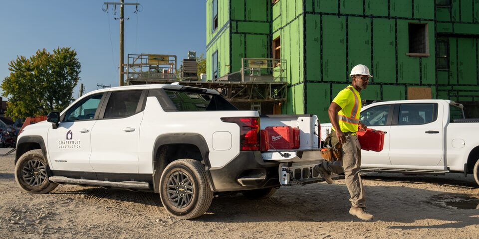 A construction worker carries tools from the back of a Chevrolet SIlverado EV tailgate.
