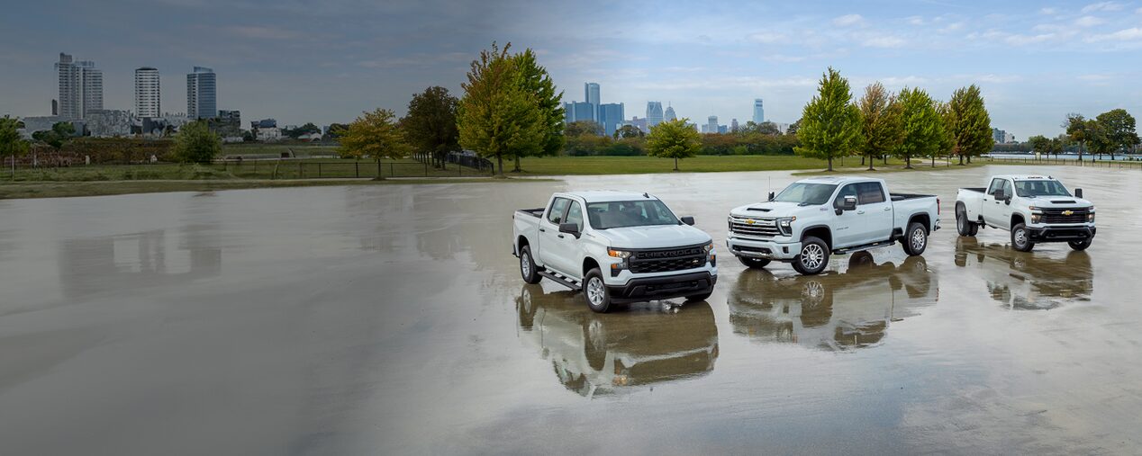 Three white Chevrolet Silverados parked in a large wet parking lot. 