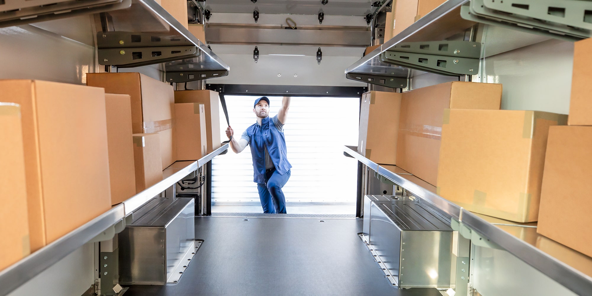 A delivery driver exiting a parked BrightDrop Zevo with a package.