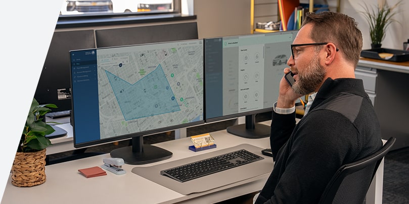 A worker on the phone, while data from the OnStar API is displayed on their monitor.