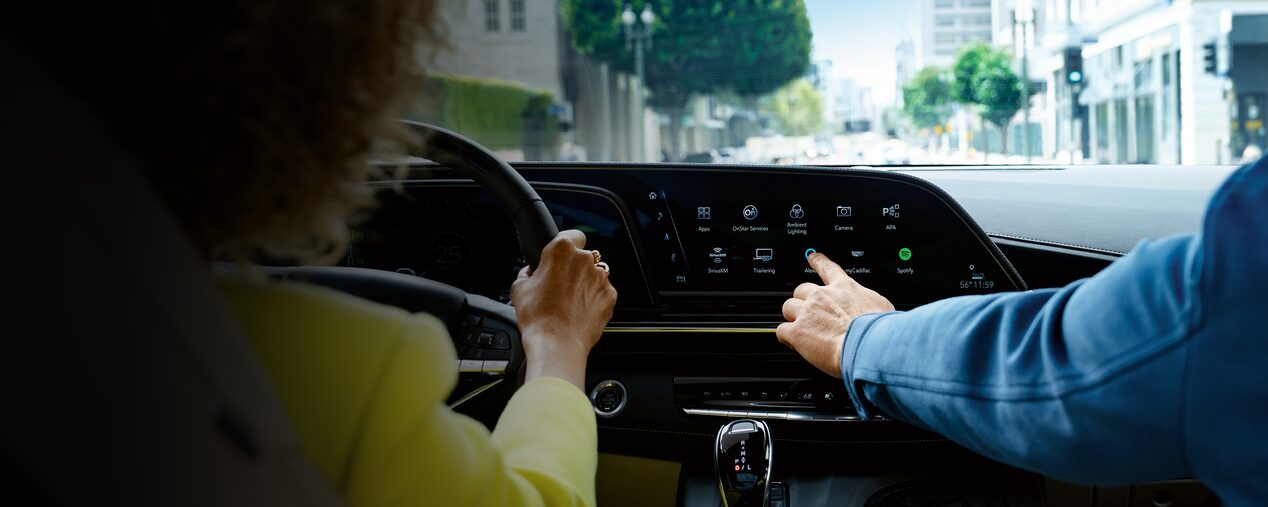 Two people driving in a GM Envolve EV. The passanger is interacting with the touch screen dashboard.