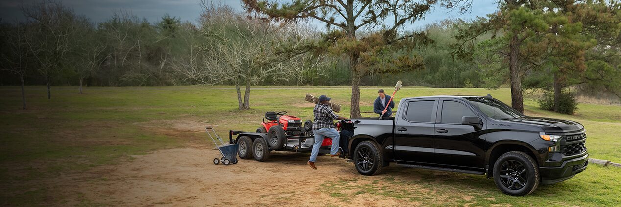 A black Chevrolet Silverado pulling a trailer with lawn equipment