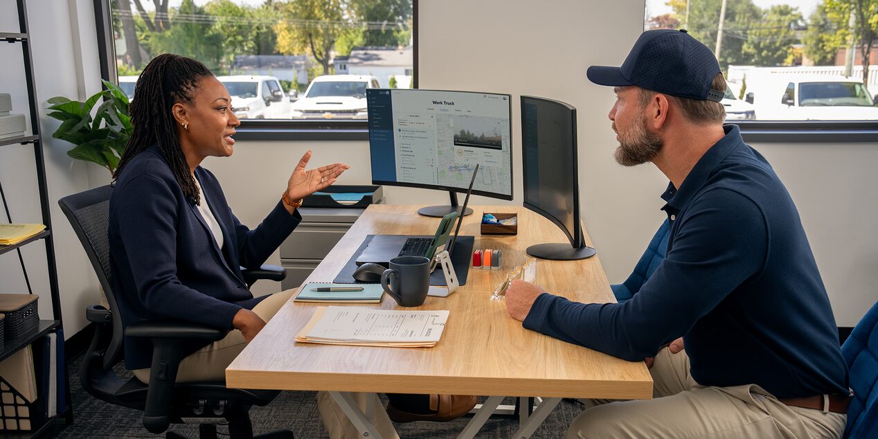 Two people speaking in an office with OnStar Vehicle Insights open on their screen