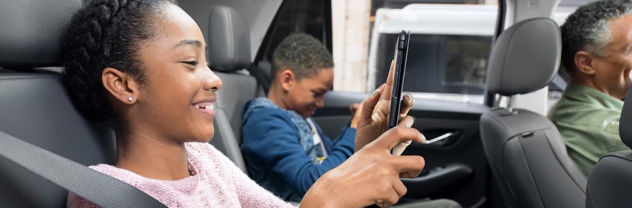 A Boy and a Girl in Backseat of Car Smiling and Watching tablets
