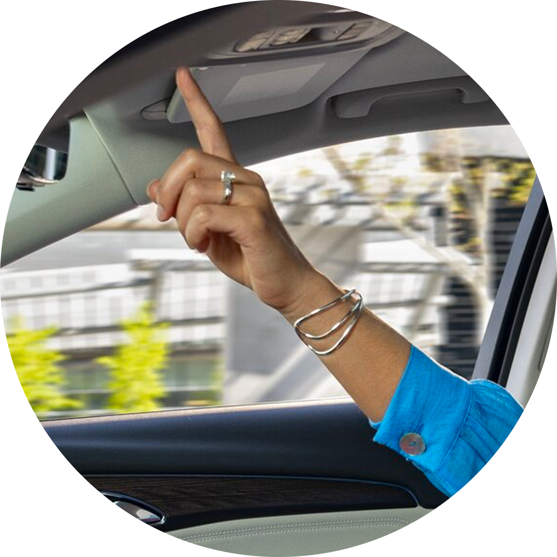 A woman's arm reaching up and touching a buttom on the roof of her vehicle.