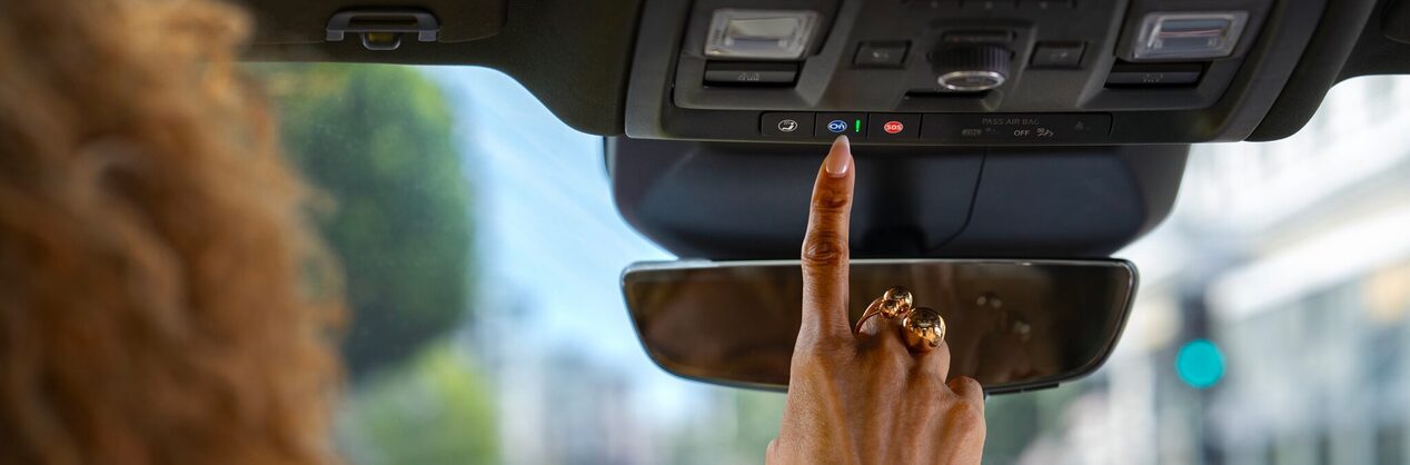 A woman's hand touching the OnStar services button in her vehicle