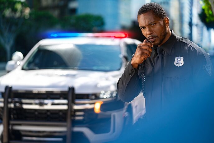 A male police officer speaking into his two way radio standing in front of his police vehicle
