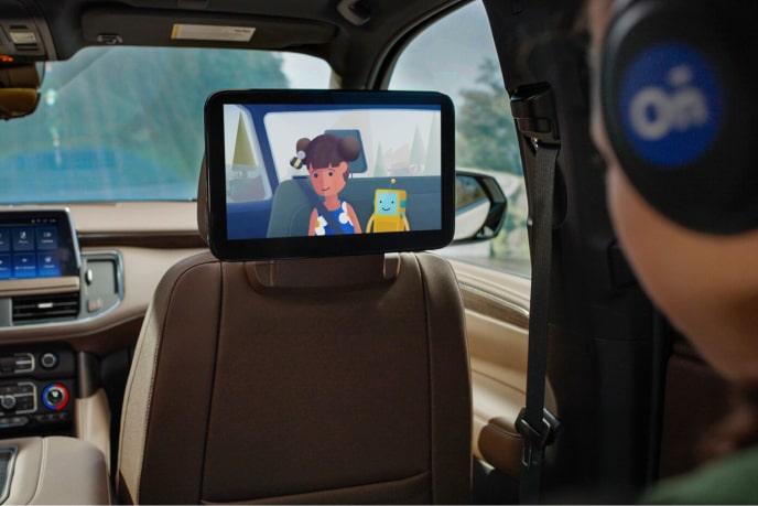 A kid is wearing headphones in the passenger seat while watching cartoons on the display attached to the front seat of the vehicle.