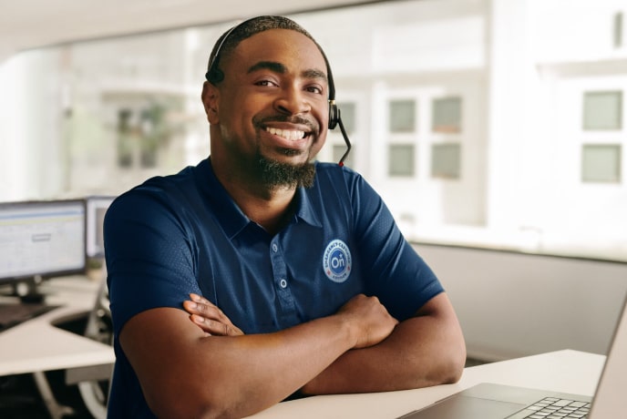 A man with arms folded in a call center desk smiling.