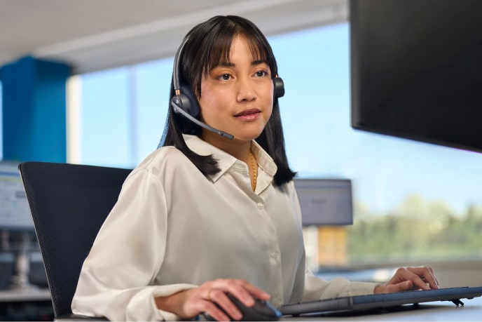 A woman wearing headphones in a call center on a computer desk helping customers.