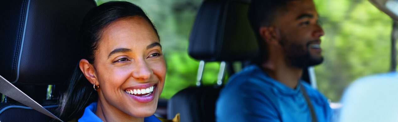 A woman looking out towards the window from the passenger seat and smiling.