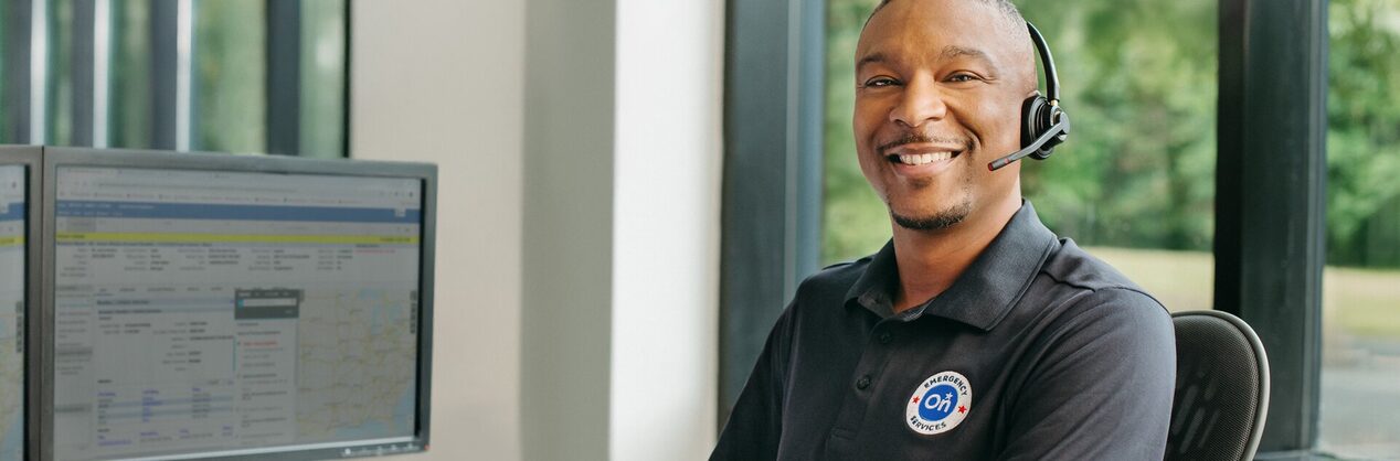 A male OnStar service advisor sitting at his desk smiling and wearing his headset